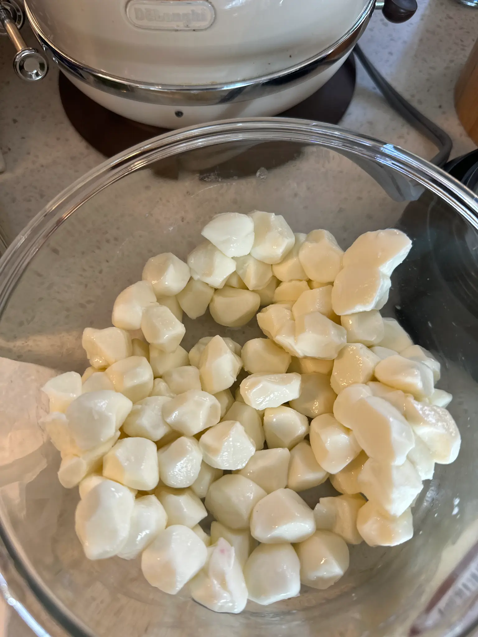 Fresh mozzarella balls cut into pieces in a glass bowl