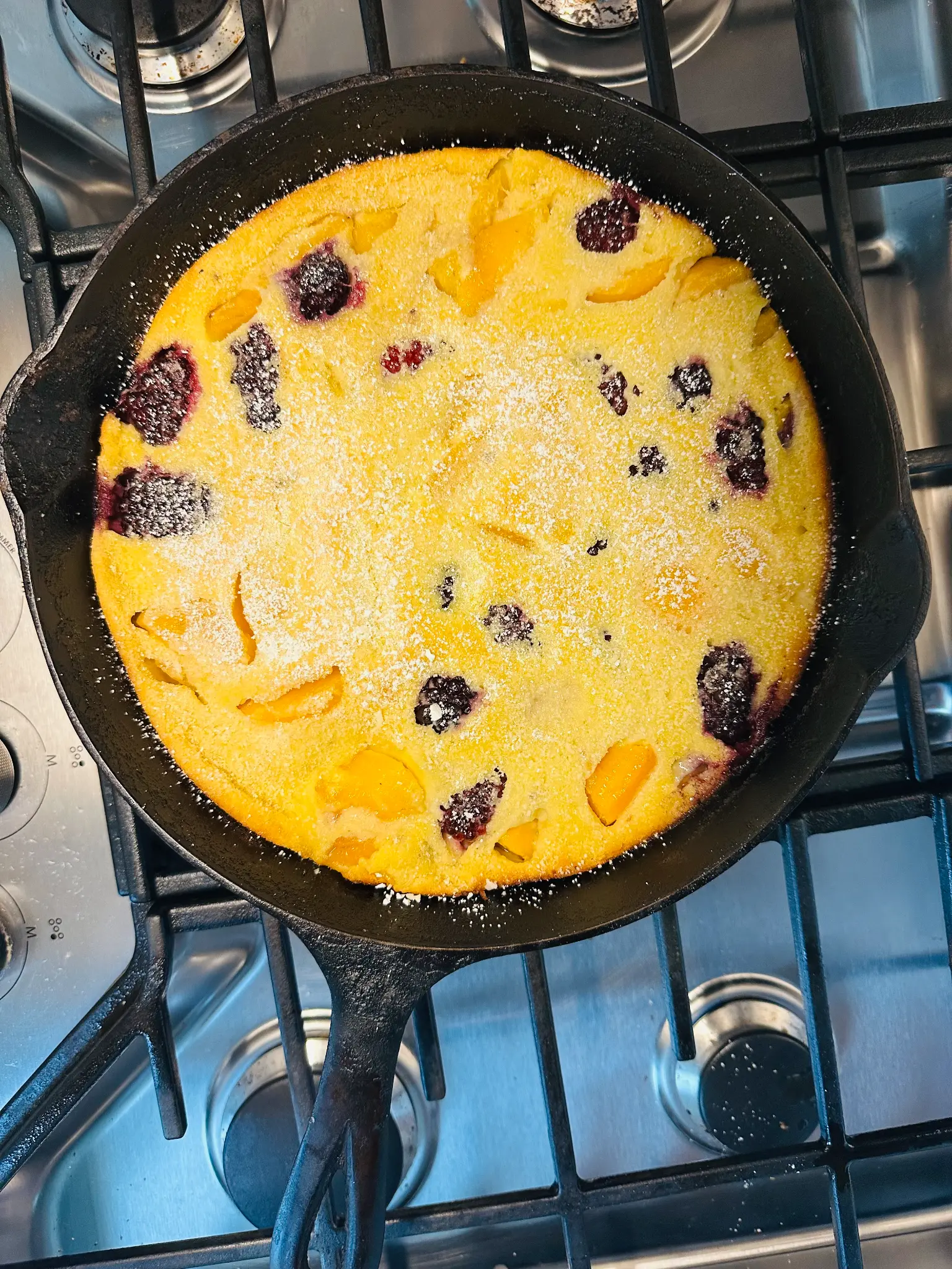 Dutch Baby in a cast iron skillet with fresh boysenberries and canned peaches, dusted with powdered sugar