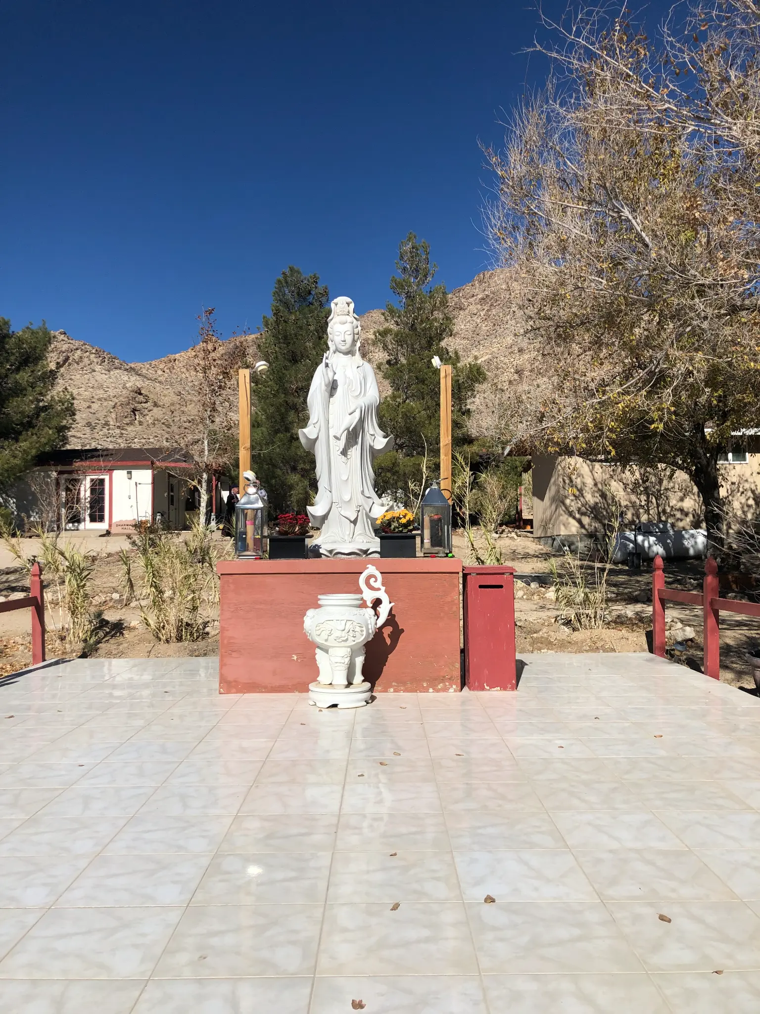 Guanyin statue at the Buddhist temple in Lucerne Valley — white bodhisattva figure on a red altar against desert mountains and blue sky