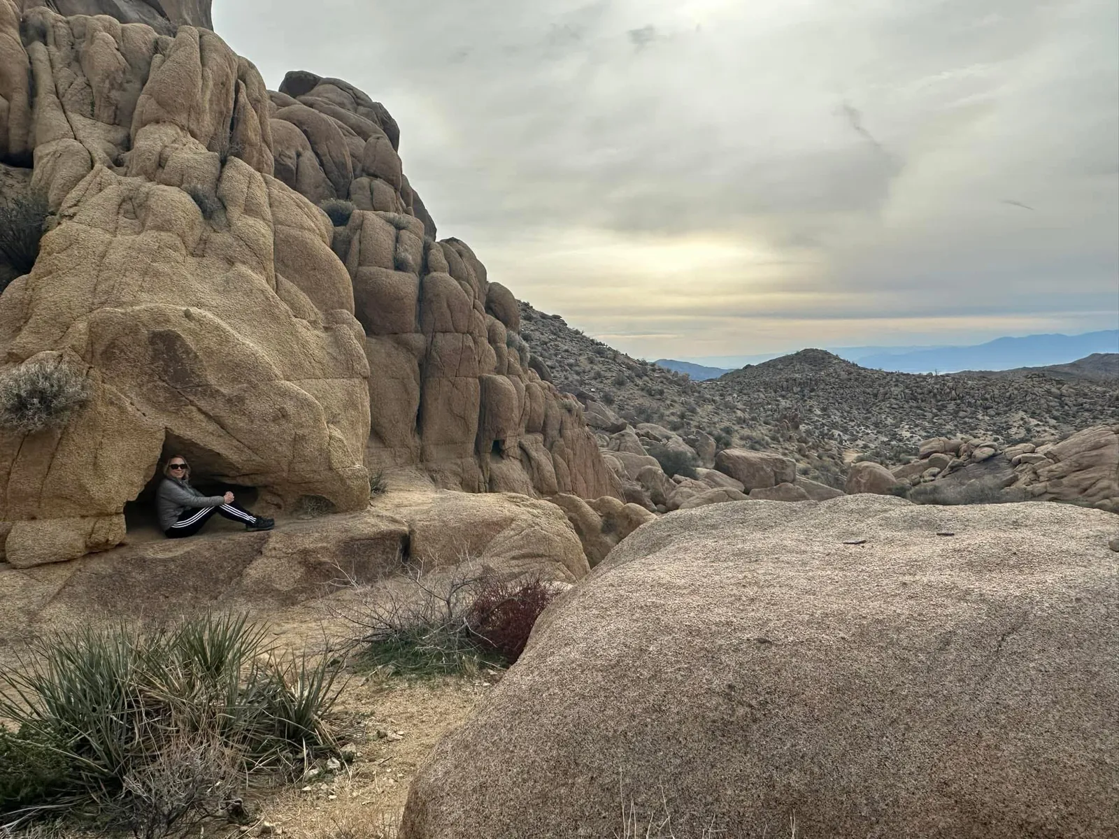 Kristen Shepherd sitting inside a rock alcove in the desert, looking out at the vast landscape — Joshua Tree, California