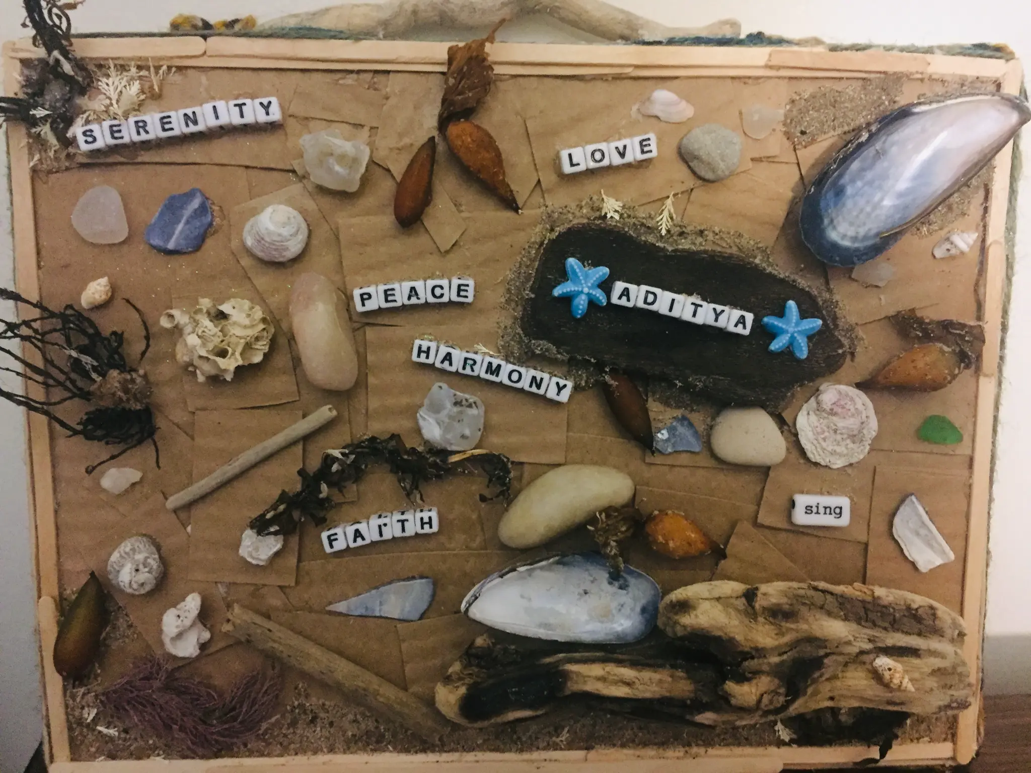 A handmade collage board with shells, stones, and words: Serenity, Love, Peace, Harmony, Faith