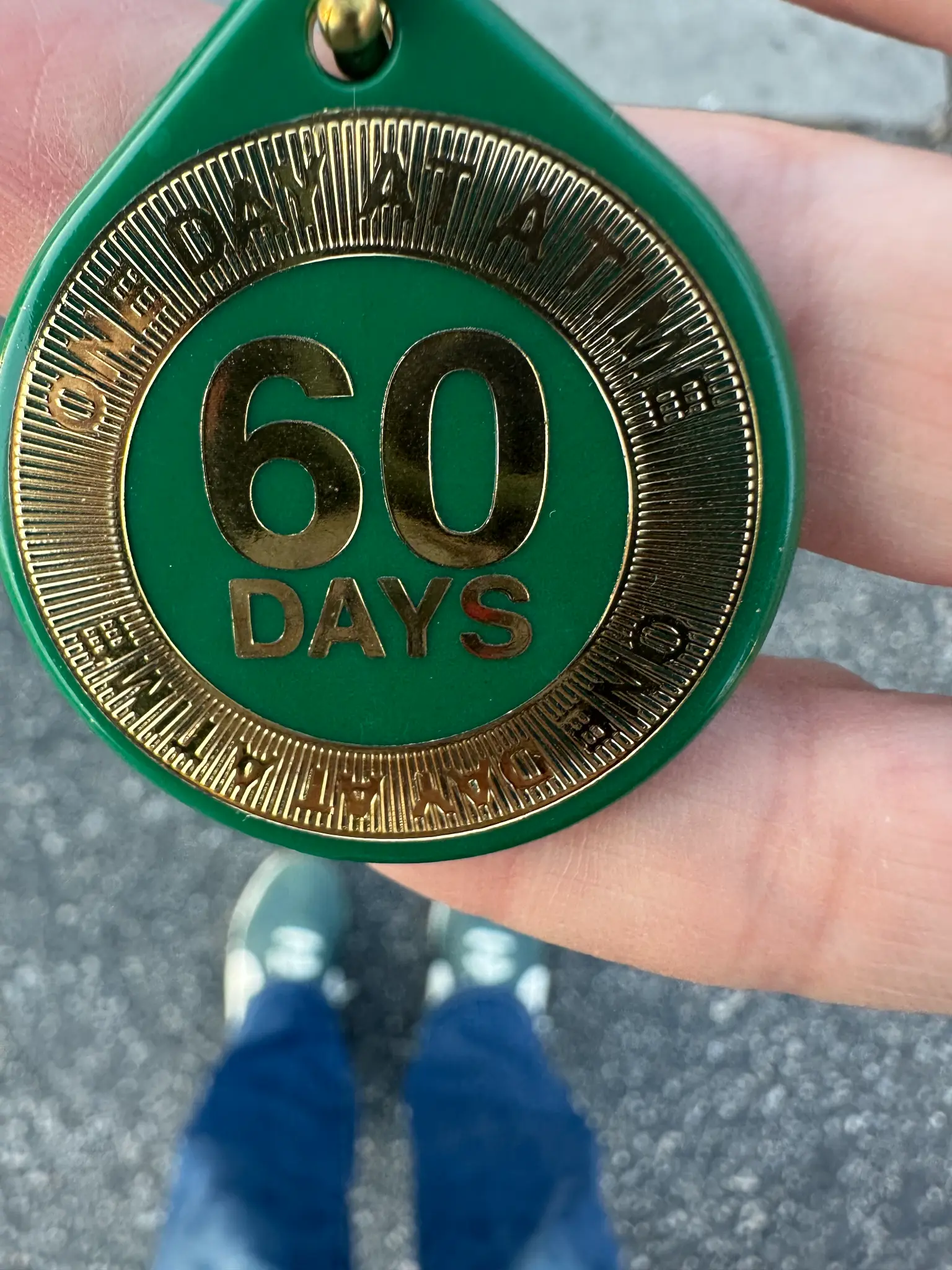 Kristen's hand holding a green and gold 60-day sobriety chip — Part Fifty-Four hero