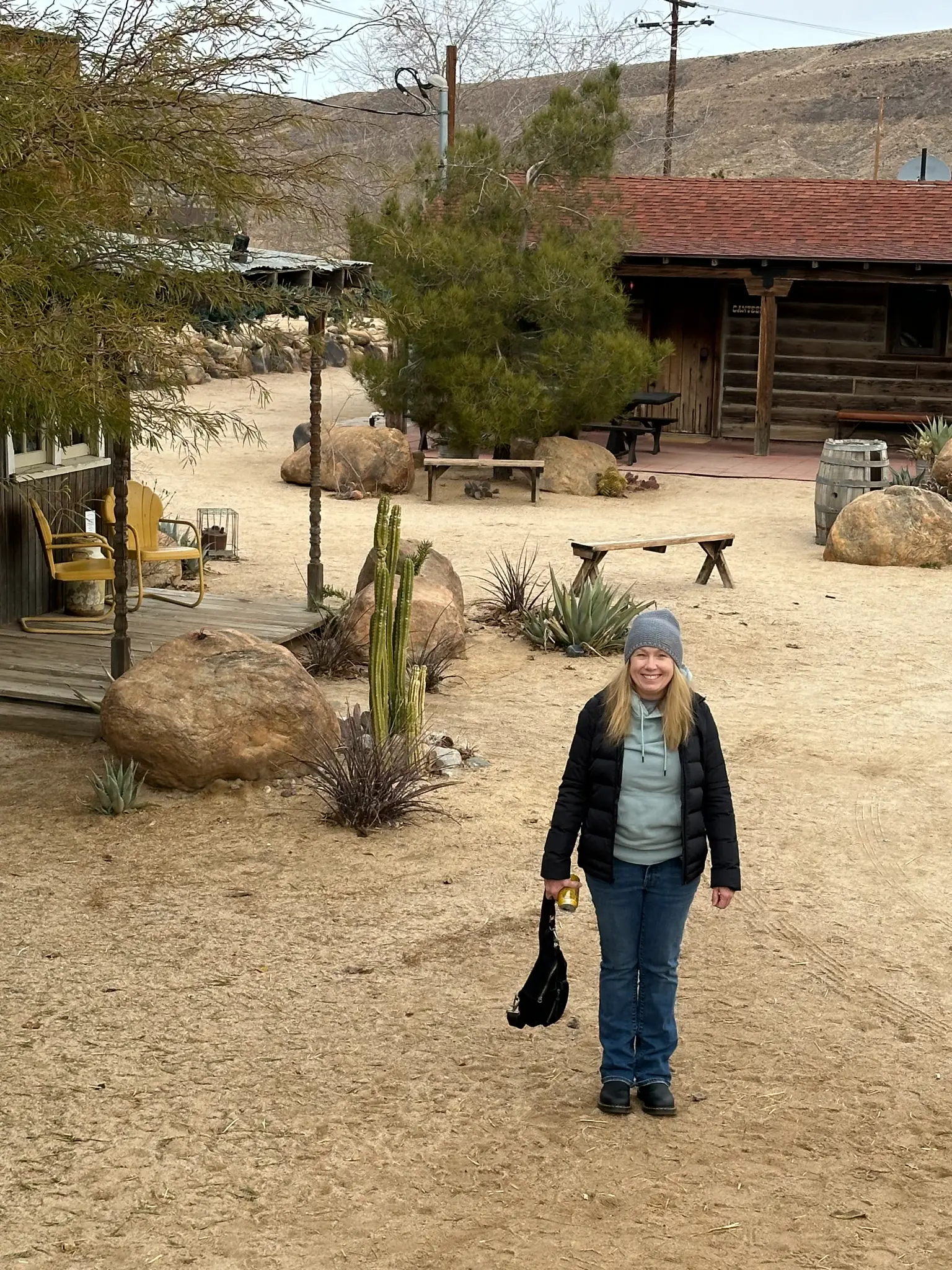 Kristen Shepherd standing in the sandy courtyard at Pappy and Harriet's Pioneertown with desert cabins and cactus behind her